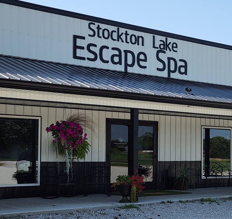 The Stockton Lake Escape Spa storefront on Highway 39 in Stockton, Missouri, with hanging flower baskets by the front door